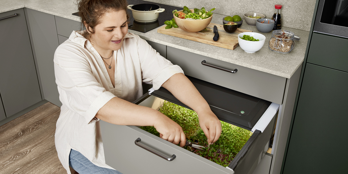 Groener wonen in de stad. Mineraalgroene elementen met grijze accenten geven de keuken een moderne natuurlijkheid. Inclusief een goed idee dat het dagdagelijkse leven in de stad wat duurzamer maakt: het ladesysteem met geïntegreerde plantverlichting plus Gardening Box   thuis telen voor stadsbewoners.